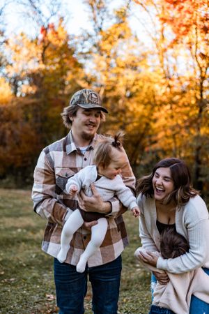 Heartwarming family moment captured in autumn forest with vibrant orange foliage in background.