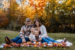 Family sitting on blanket surrounded by fall leaves during outdoor autumn photo session.