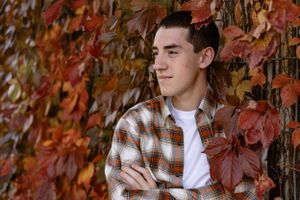 Portrait of young man in plaid shirt against wall of red autumn leaves.