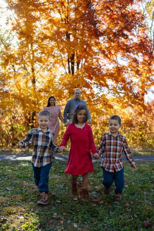 Group of children holding hands while walking together through vibrant autumn foliage in a park.