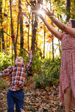 People joyfully playing with falling autumn leaves in golden sunlit forest.