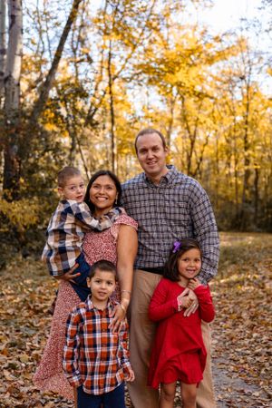 Family posing together on a leaf-covered path surrounded by golden autumn trees.