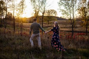 Couple holding hands while walking through field at sunset with golden light.