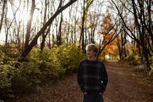 Person standing on forest path with sunlight filtering through autumn trees.
