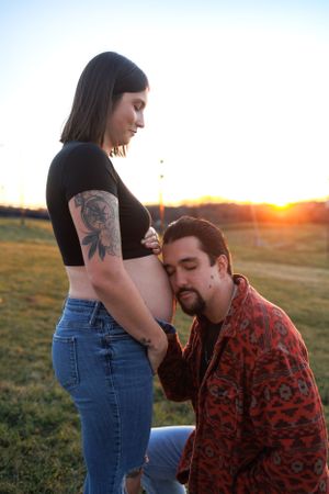 Expectant couple shares tender moment during sunset maternity photoshoot outdoors.
