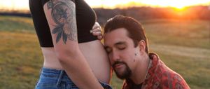 Intimate maternity photo of couple at sunset in field with visible tattoo art.