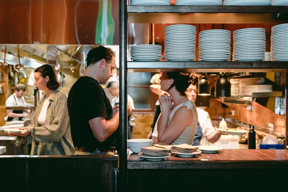 Restaurant staff working behind a busy counter with stacked plates on shelves.