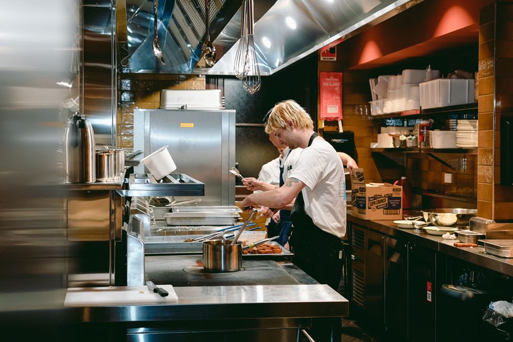 Chef working at a stainless steel commercial kitchen station with pots and equipment.