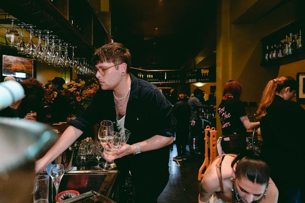 Bustling bar scene with people serving drinks under dim lighting.