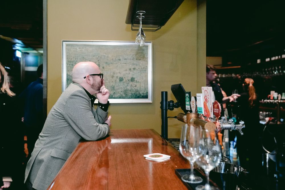 Customer sitting at bar counter looking at drink menu in dim lighting.