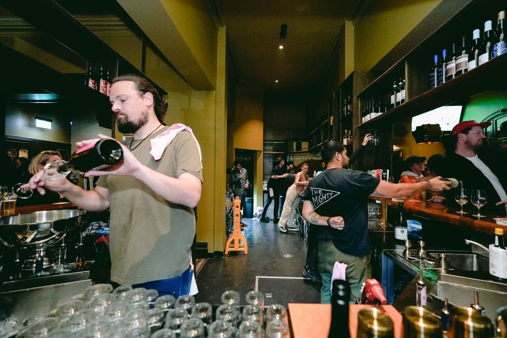Bartenders preparing drinks behind counter with rows of empty glasses.