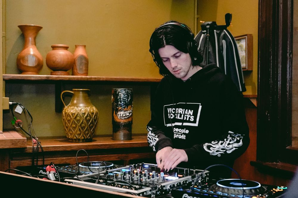 DJ operating mixing equipment with decorative vases on shelves in background.
