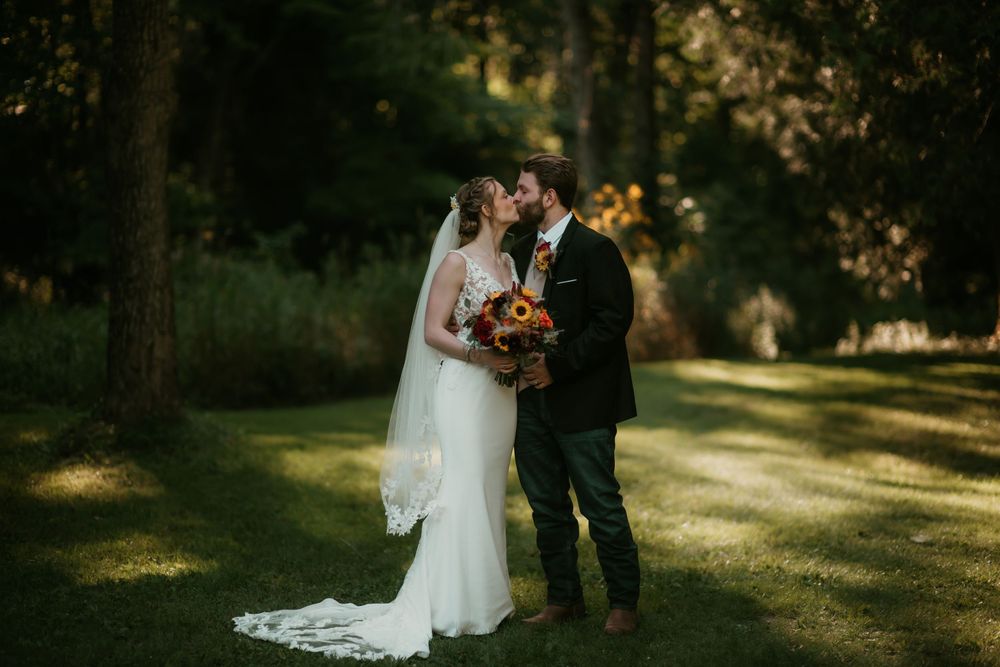 A couple in wedding attire shares a romantic moment in a sunlit forest setting.