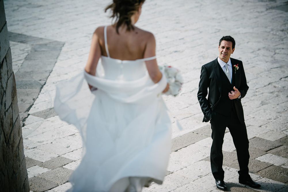 Bride in flowing white dress walking with others on stone pavement.