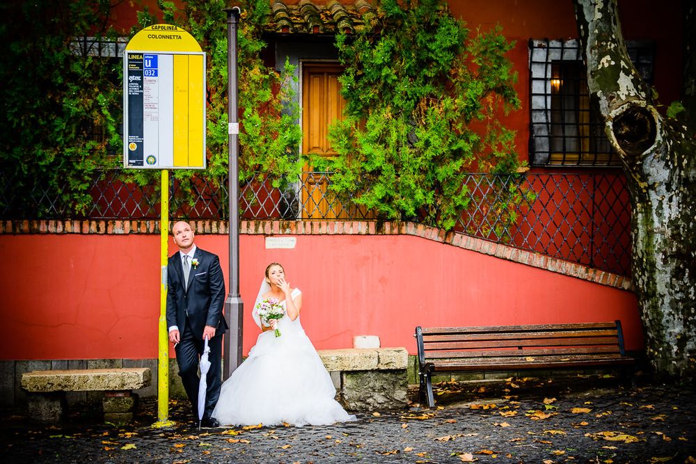 Wedding couple poses against vibrant red wall with green foliage and yellow accents.