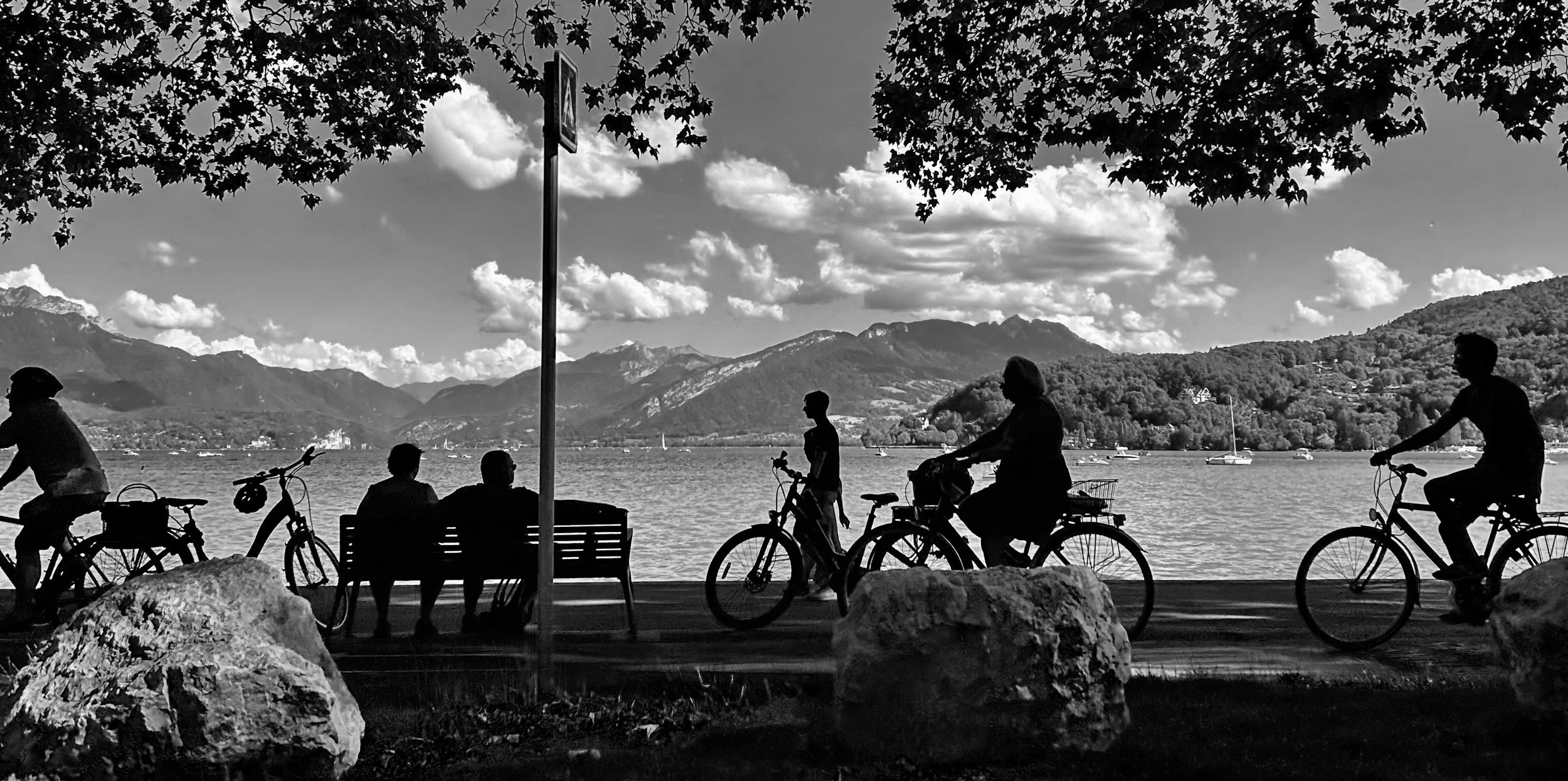 A photograph of Lake Annecy, capturing the silhouette of cyclist and pedestrians.
