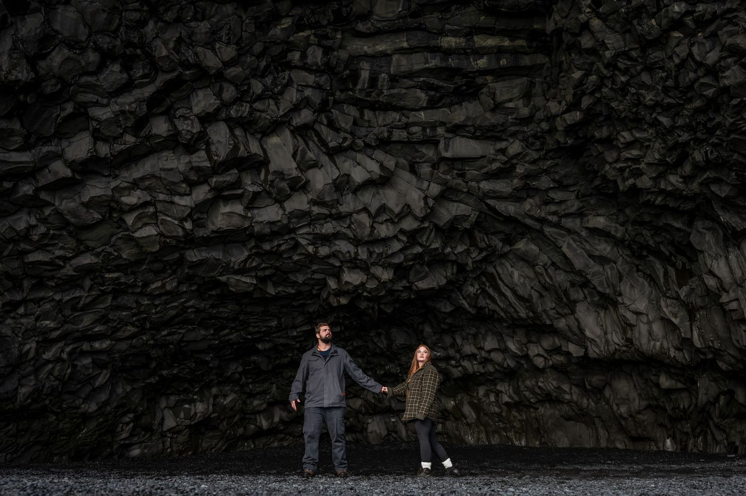 Two people standing in dramatic black basalt cave formation in Iceland.