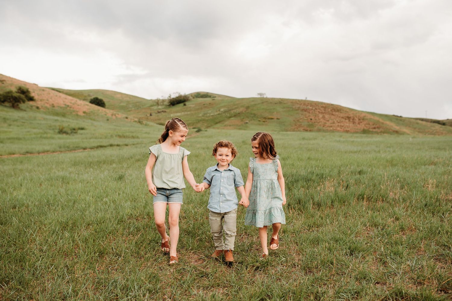 Three children walking together through green hillside meadow.