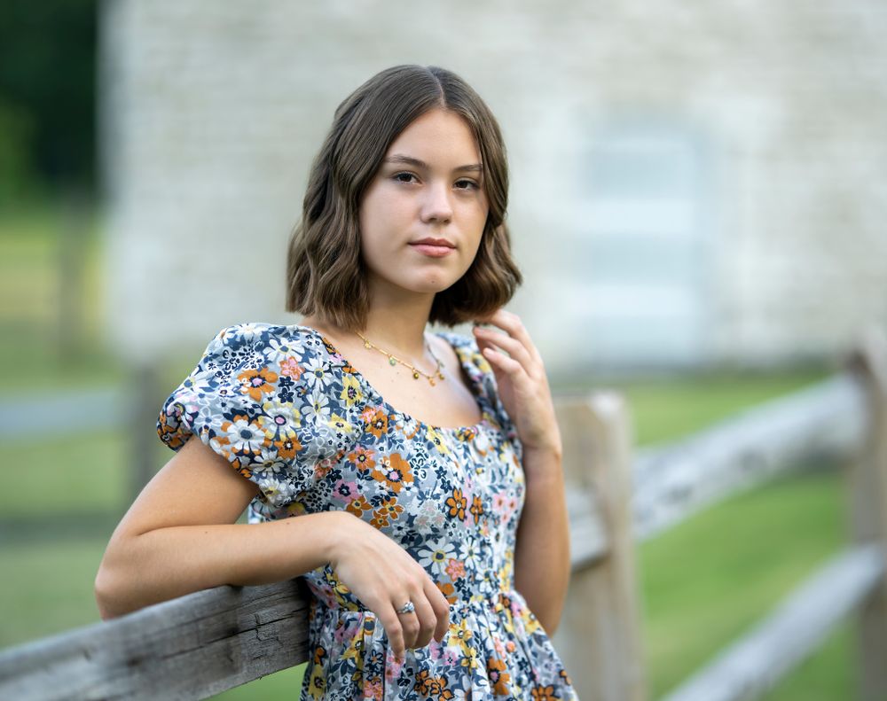Outdoor portrait in floral dress leaning against wooden fence.
