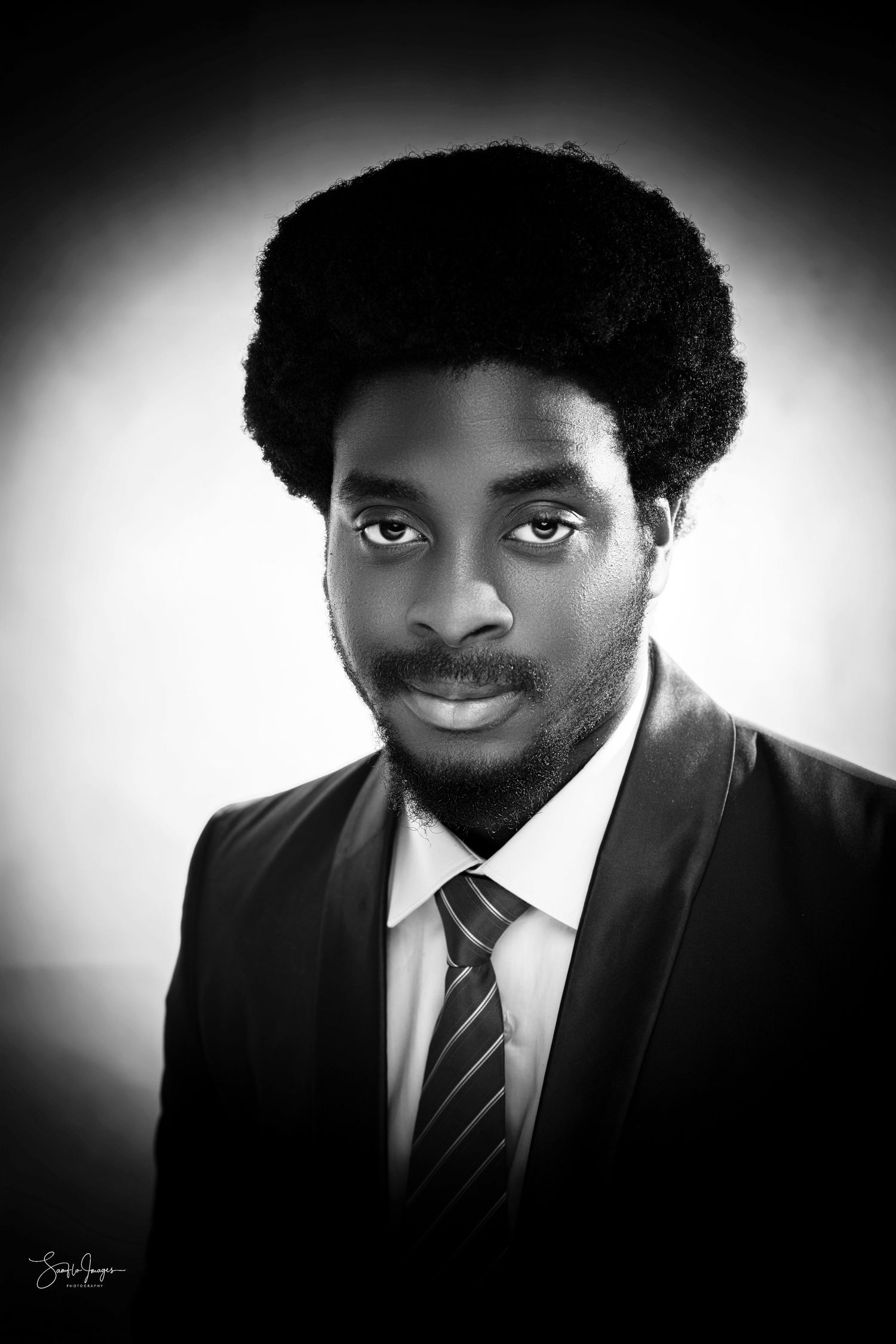 Professional black and white portrait photograph showing an elegant look with suit and tie against a dark background.