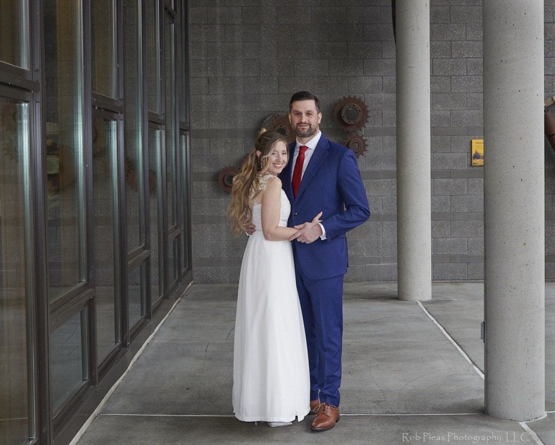 Formal of Bride and Groom standing together, holding hands under cover at Environmental Services Building in University Place, WA.
