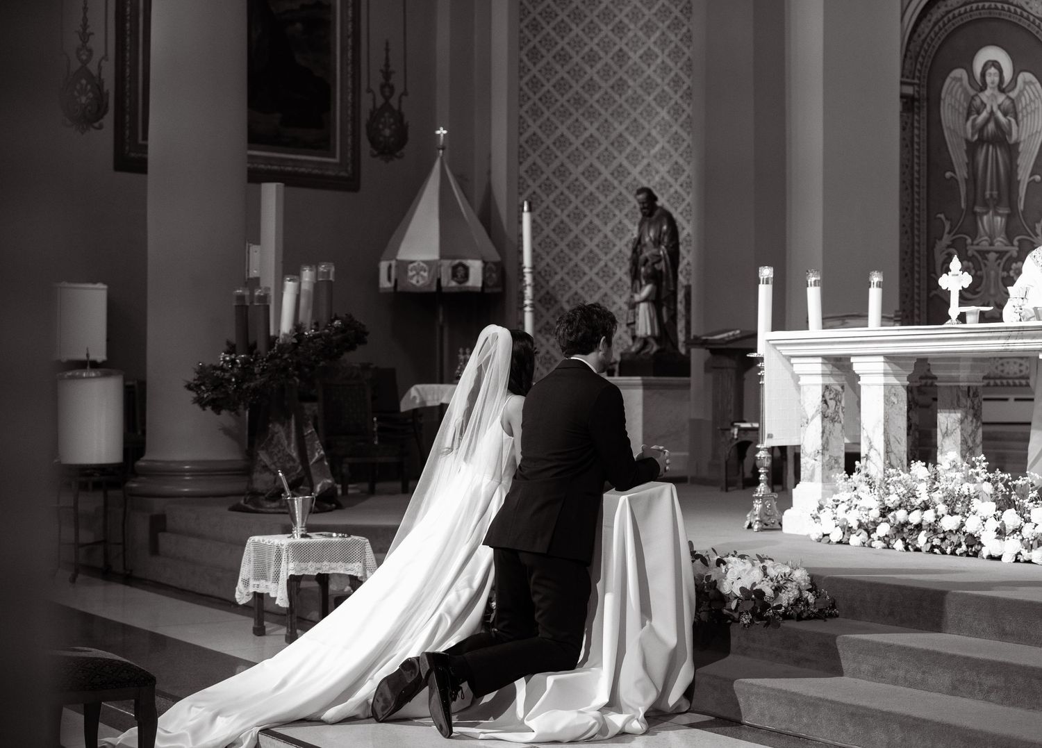 Black and white photo of a wedding ceremony in a traditional church with ornate altar decorations.