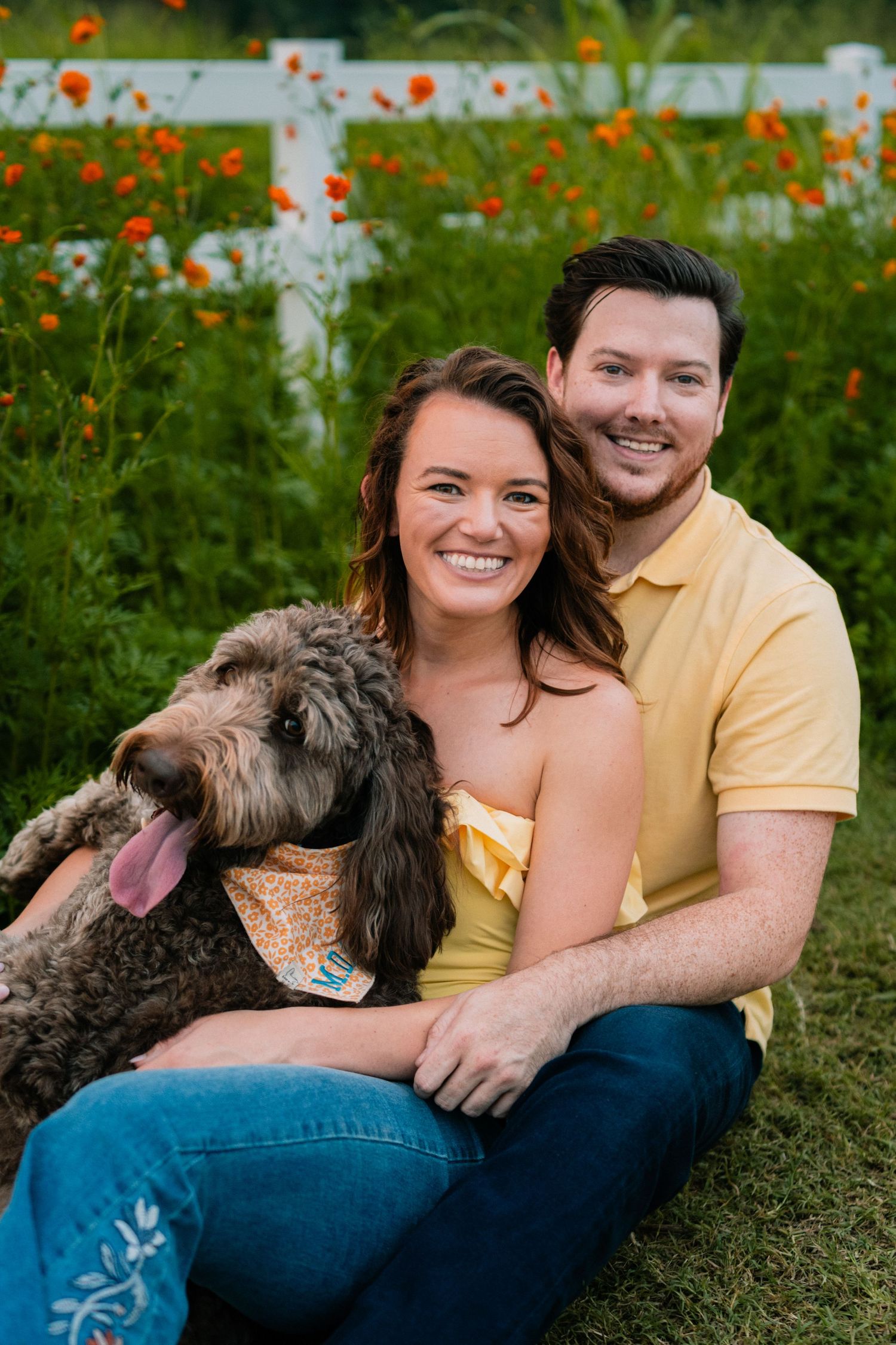 Happy couple with their large doodle dog posing in garden with orange flowers.