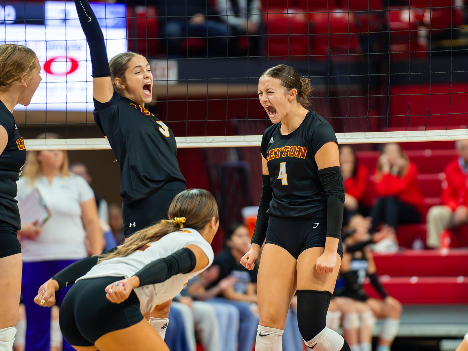 High school volleyball team celebrates enthusiastically during match in a gymnasium.