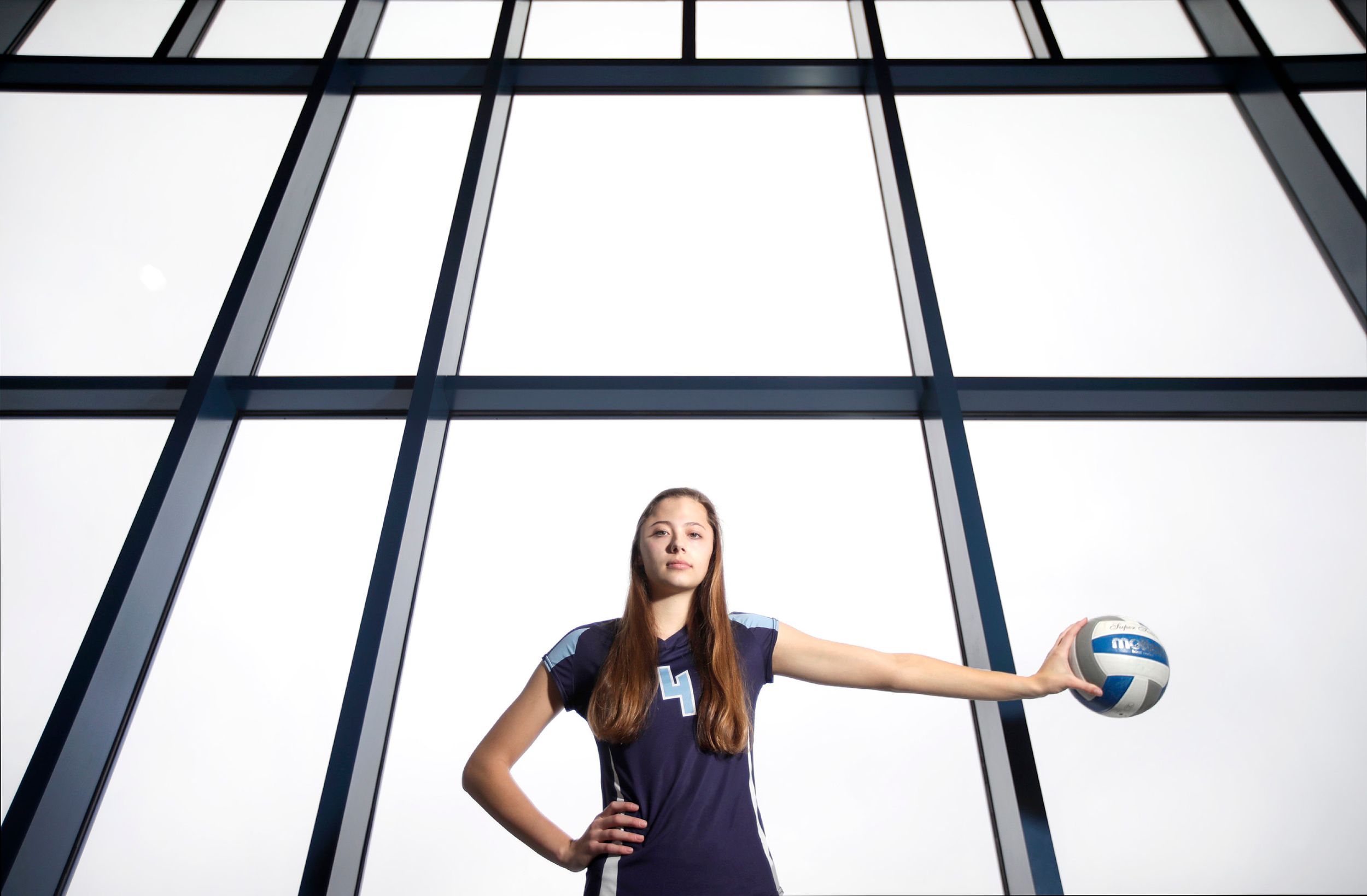 A volleyball player holds the ball to the side in front of large windows during a portrait session.