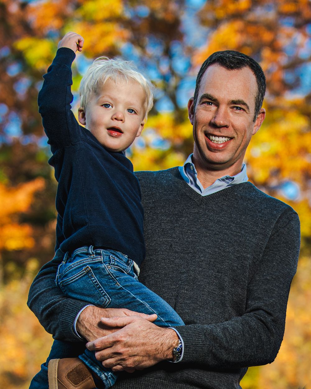 Parent and child pose together against vibrant fall foliage background.