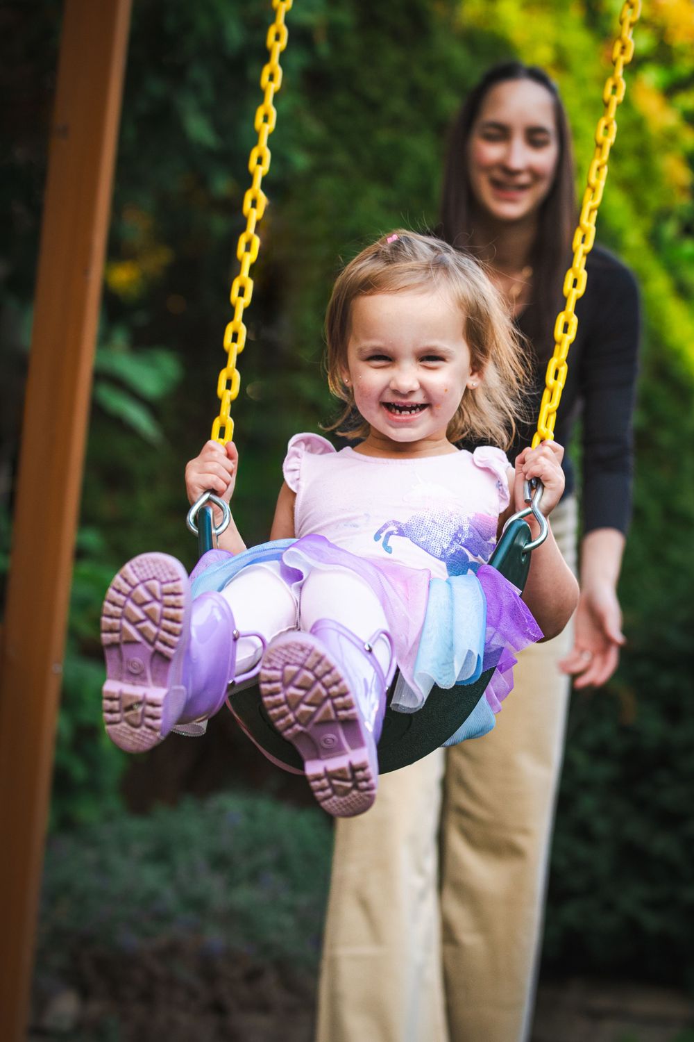 A happy child wearing a purple and pink dress swings joyfully on a yellow-chained playground swing.