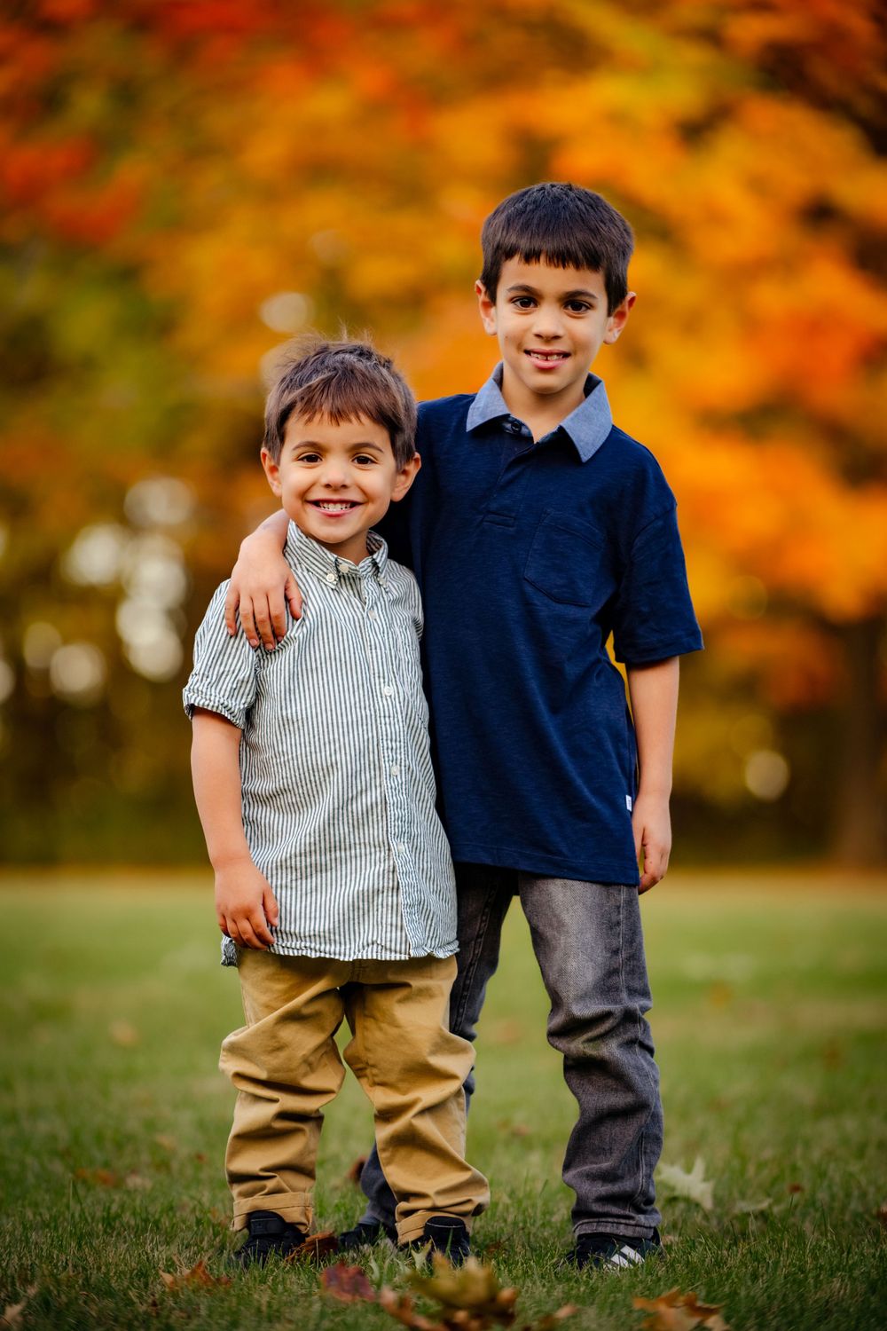 Two brothers standing together outdoors with beautiful fall foliage in background.