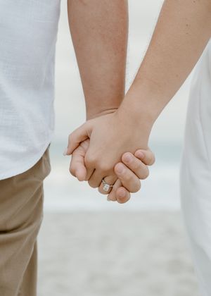 Close-up of engaged couple holding hands showing diamond engagement ring on the beach.
