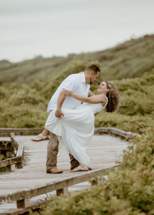 Groom dipping bride on a wooden boardwalk surrounded by lush greenery during engagement shoot.