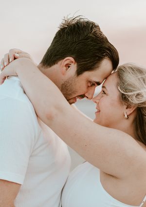 Romantic couple touching foreheads in intimate embrace on beach during golden hour sunset.