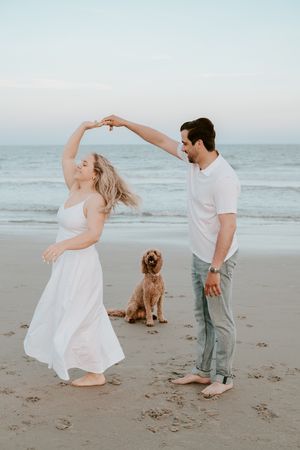 A couple dancing on the beach at sunset with their golden doodle dog sitting between them.