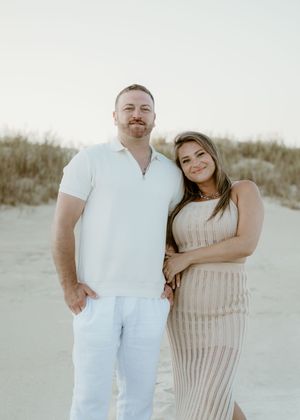 Smiling couple posing together on sandy beach dunes during golden hour engagement or maternity session.