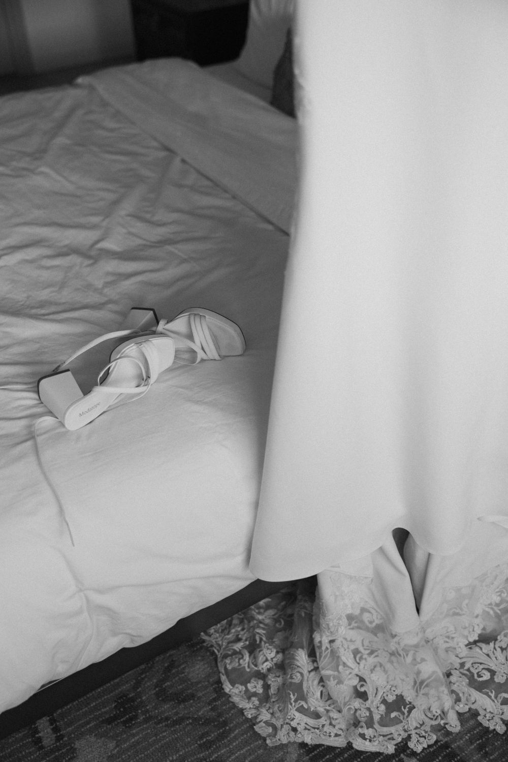 Editorial-style dress shot of Dani’s wedding dress and bridal shoes hanging on a bed frame in a Ventura county Airbnb.