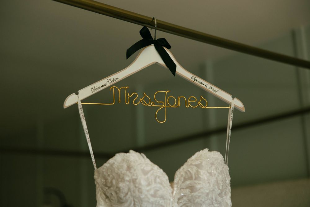 Editorial-style dress shot of Dani’s wedding dress and custom name hanger, hanging on a bed frame in a Ventura county Airbnb.