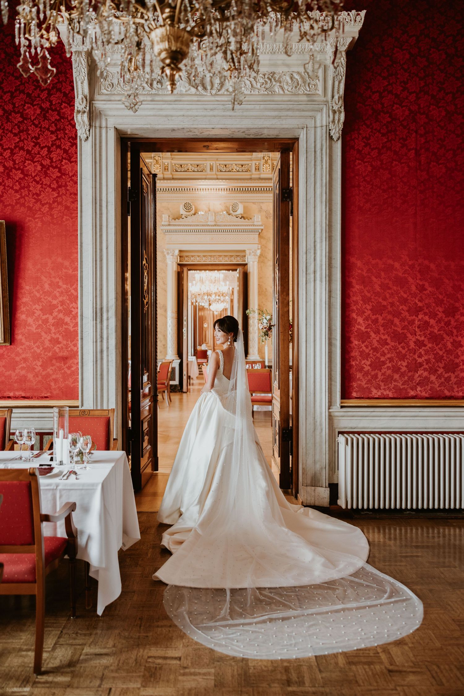Elegant wedding dress with long train in room with red damask wallpaper. Organized wedding by MyCastleWedding | Dresden. Albrechtsberg