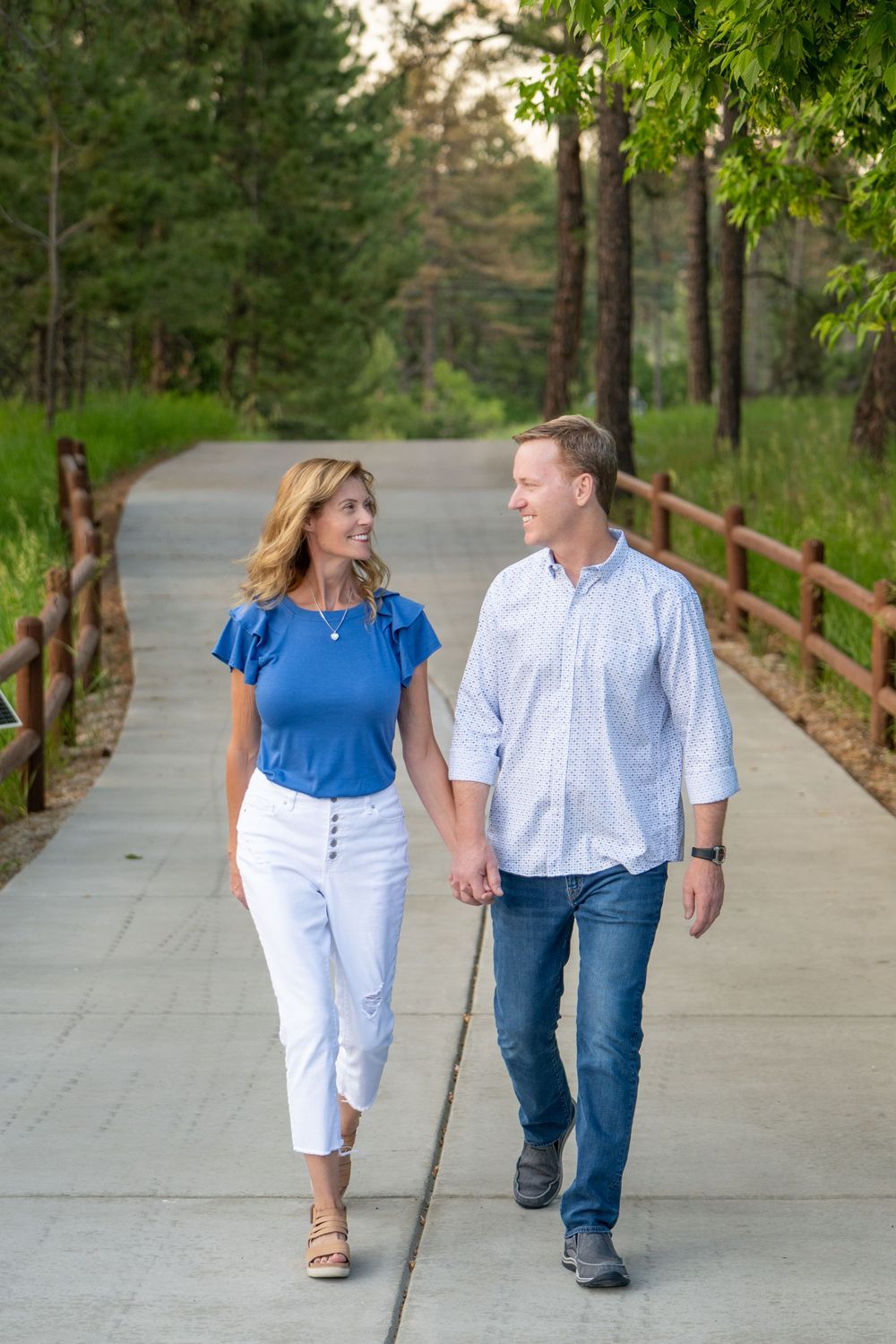 A couple in coordinating blue and white outfits walking together on a concrete path surrounded by green trees.
