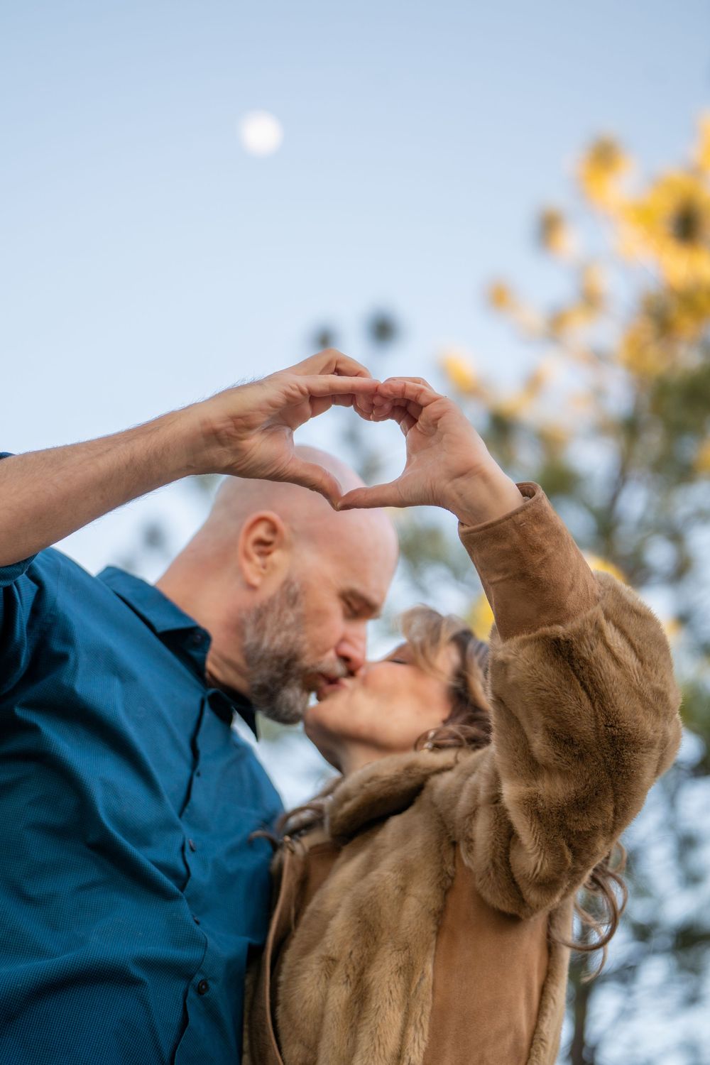 Two people embrace and dance together against a blue sky with autumn foliage in the background.