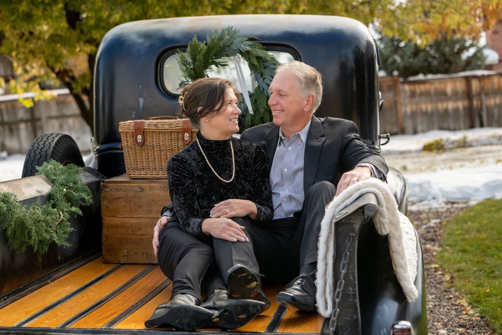 Couple sitting together in back of vintage black truck with cozy blanket and holiday decor.