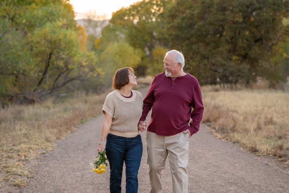 Couple walking together on dirt path with yellow flowers and autumn trees.