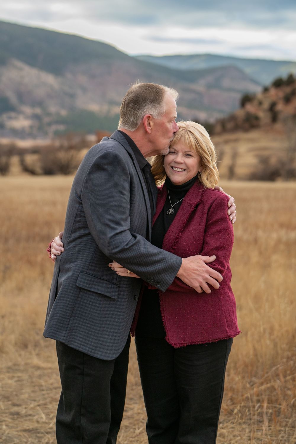 A couple shares an affectionate moment in front of a scenic mountain landscape on a golden autumn day.