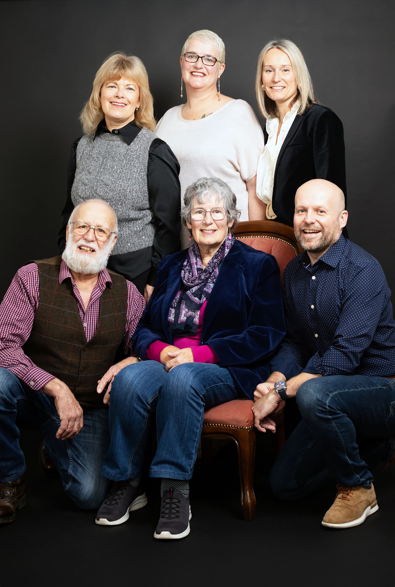 Family portrait of six people seated together against black background in casual attire.
