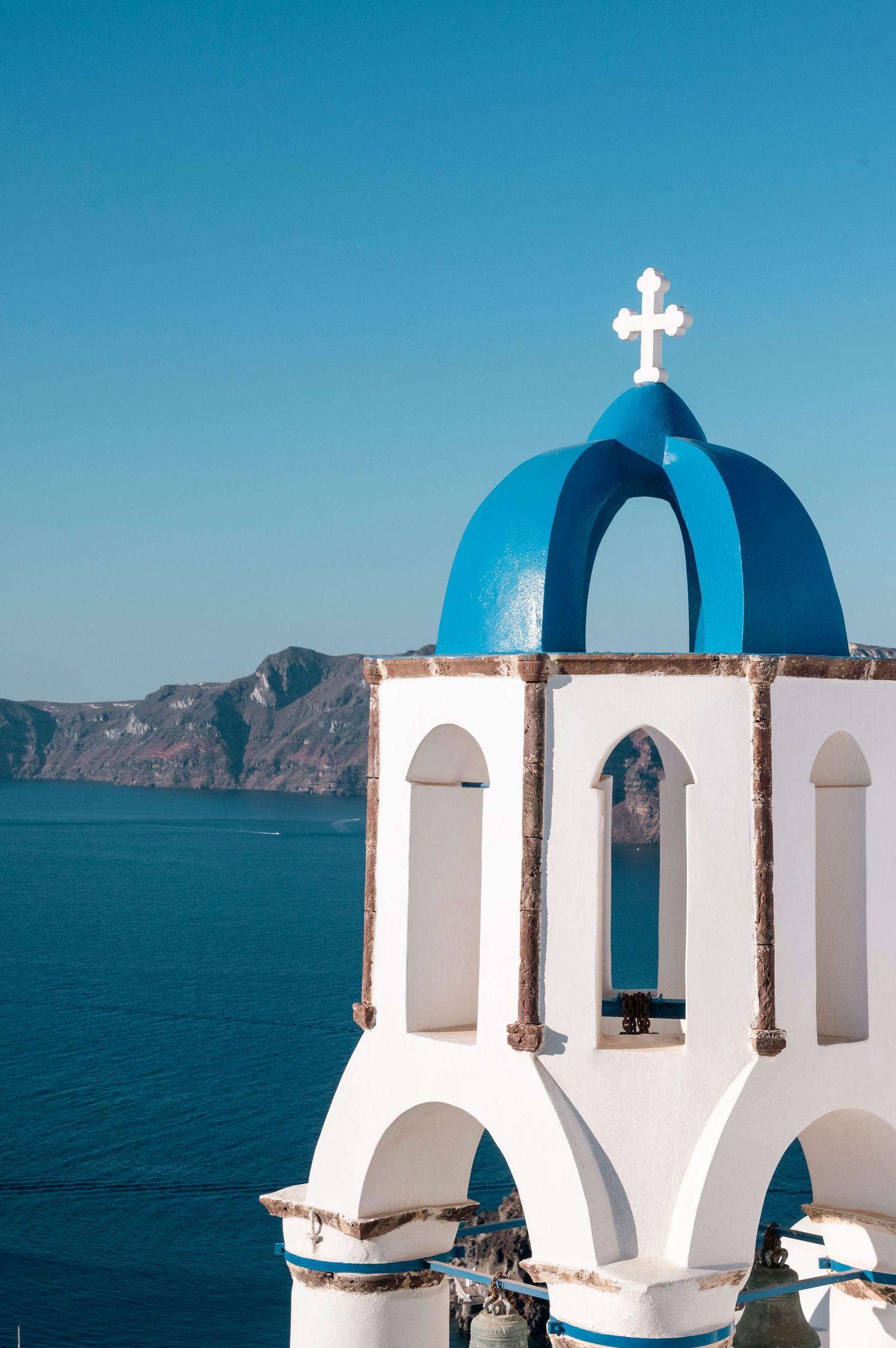 White church bell tower with blue dome against crystal clear Mediterranean waters in Santorini.