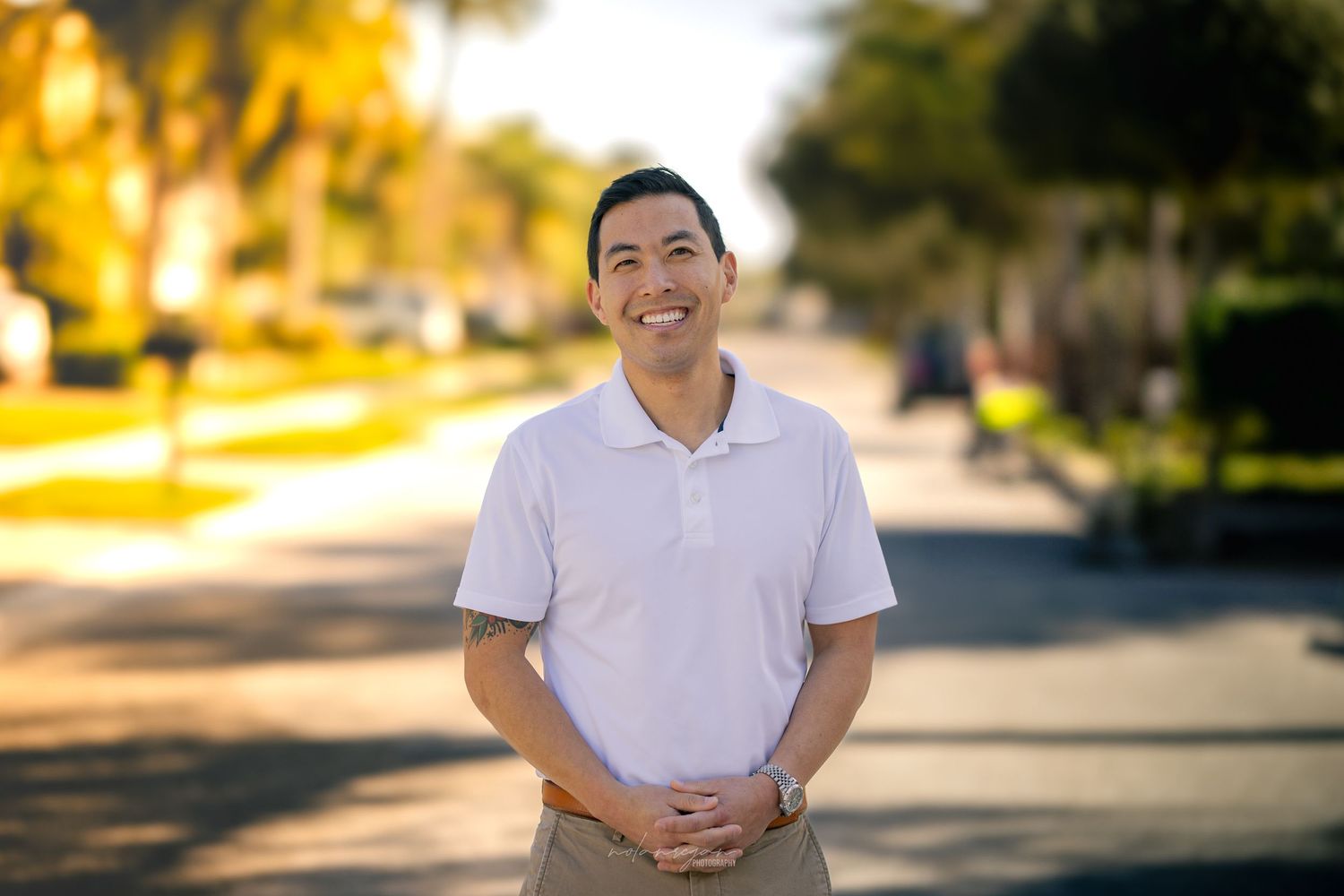Casual outdoor portrait in white polo shirt with warm sunlit background.