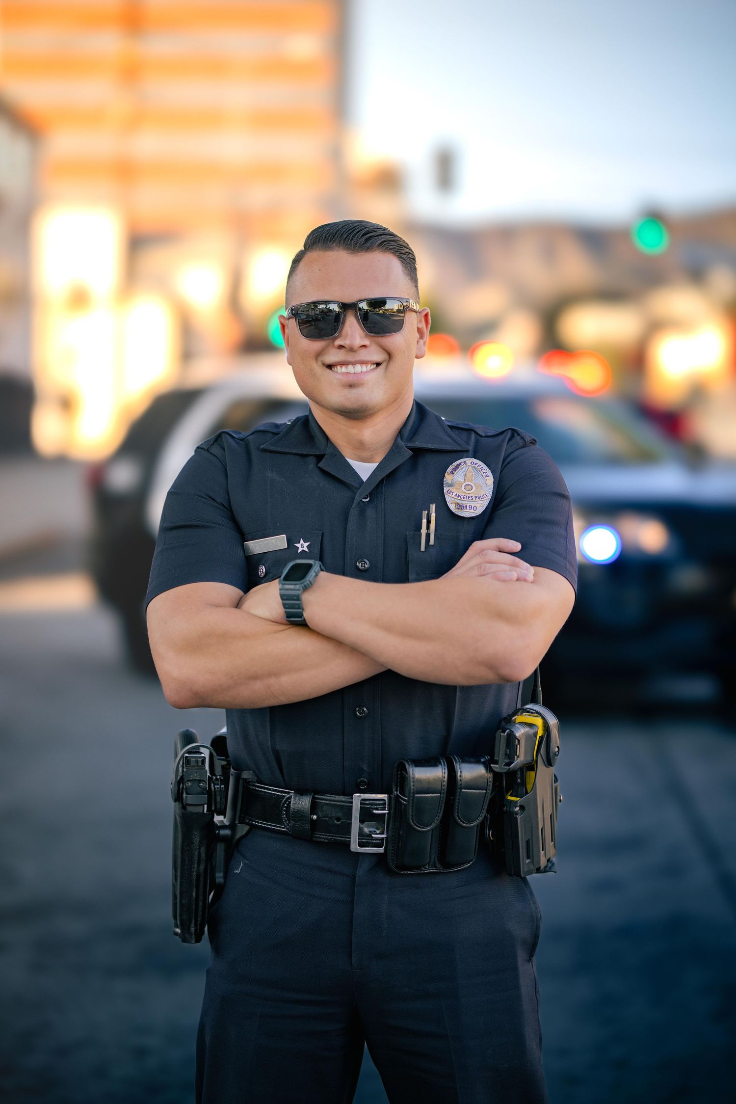 Police officer in uniform smiling and posing with arms crossed in an outdoor setting.