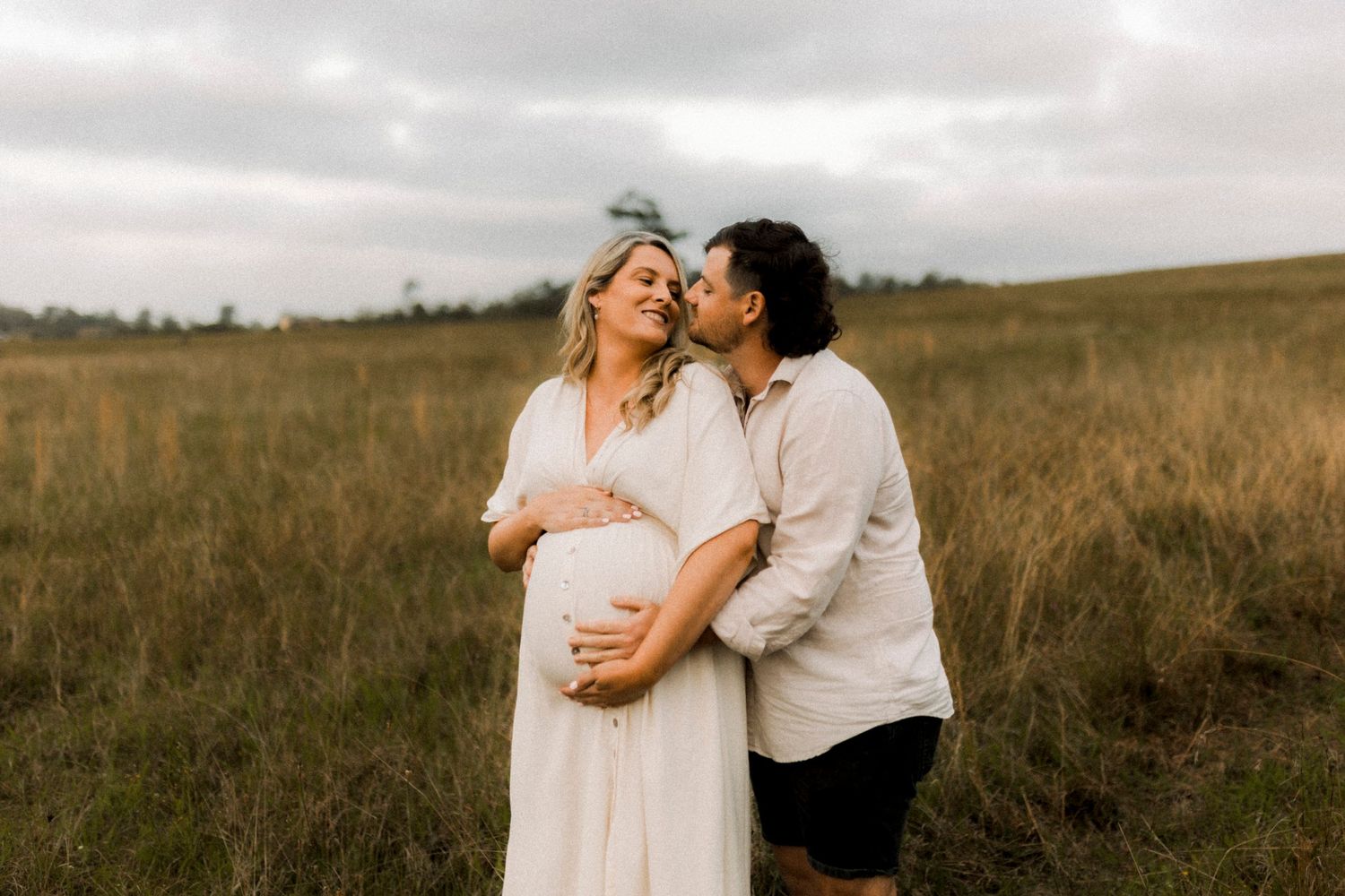 Couple embraces during sunset maternity shoot in rustic field.